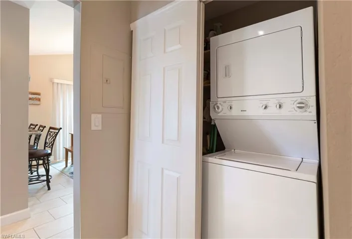 Washroom with estacked washer and dryer, electric panel, and light tile patterned floors