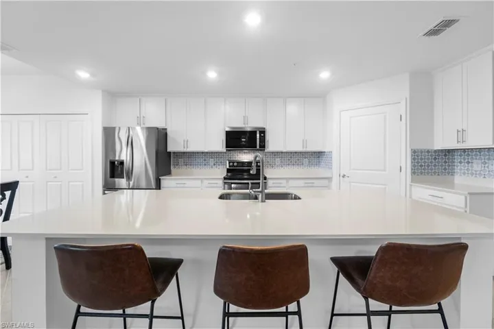 Kitchen featuring a large central island with a solid-surface countertop, white shaker-style cabinetry, stainless steel appliances, and a decorative tile backsplash