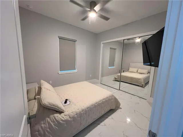Bedroom featuring expansive mirrored closet doors, a ceiling fan with integrated lighting, and a single window with a roller shade