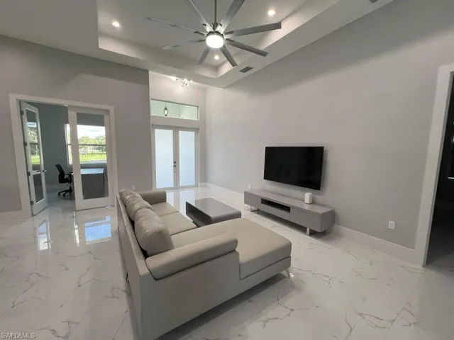 Spacious living area featuring high ceilings with tray detailing and a contemporary ceiling fan