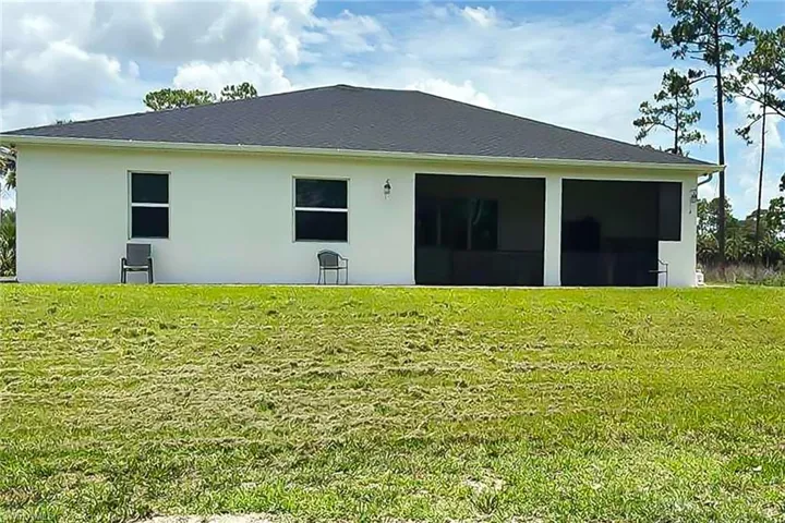 Rear exterior of a single-story residence featuring a white stucco facade and a dark shingle roof