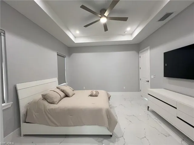 Spacious interior featuring a tray ceiling with recessed lighting and a ceiling fan, large format white tile flooring, and a white paneled door with dark hardware