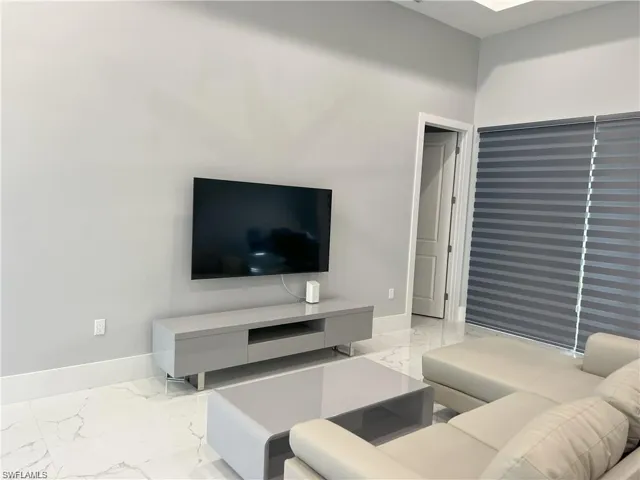 Spacious room featuring light gray walls, large format white tile flooring with gray veining, wide white baseboards, and a white interior door frame