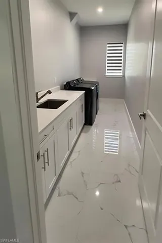 Laundry room featuring white cabinetry, a countertop, an under-mount sink with a faucet, and patterned tile flooring