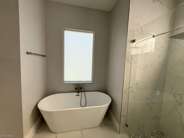 Freestanding soaking tub with chrome fixtures under a privacy window