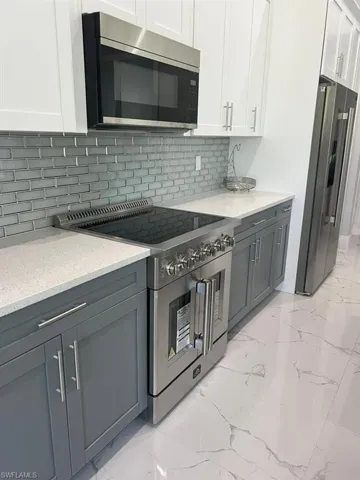 Contemporary kitchen featuring a stainless steel range, white quartz countertops, subway tile backsplash, white upper cabinetry, and gray lower cabinetry