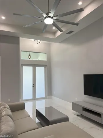 Spacious living area featuring high tray ceilings with recessed lighting, a large ceiling fan, and polished marble-look flooring