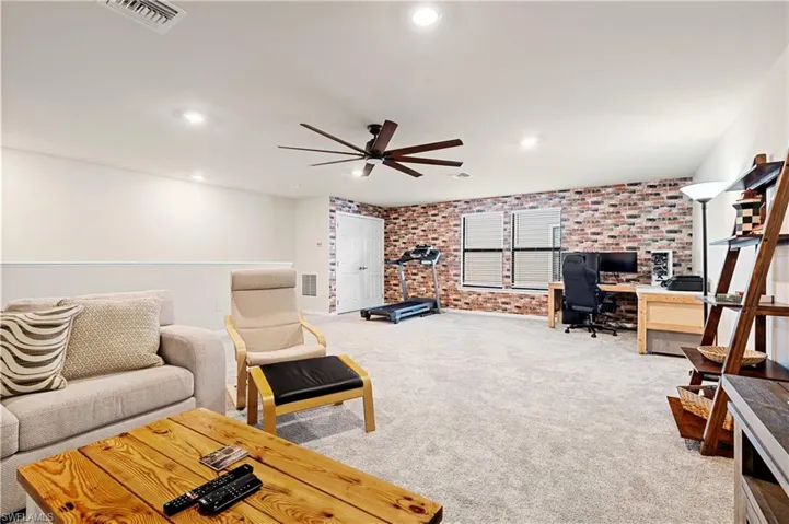 Living room featuring brick wall, an office area, light colored carpet, a ceiling fan, and recessed lighting