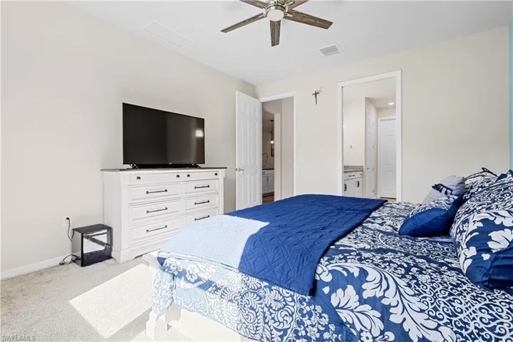 Bedroom featuring light colored carpet, ceiling fan, ensuite bathroom, and attic access