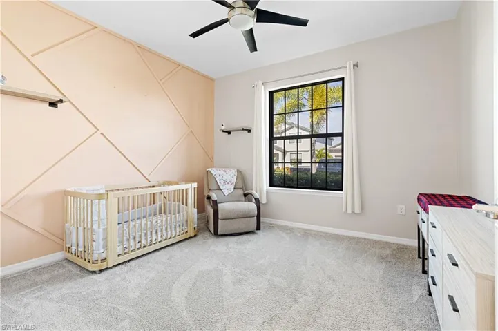 Bedroom featuring a crib, light colored carpet, ceiling fan, and a decorative wall