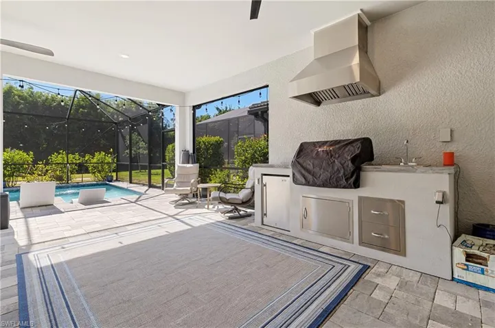 View of patio / terrace with a sunroom, an outdoor kitchen, an outdoor pool, a ceiling fan, and glass enclosure