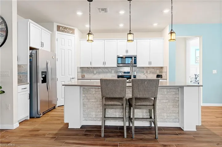 Kitchen featuring appliances with stainless steel finishes, white cabinets, an island with sink, decorative light fixtures, and a kitchen bar