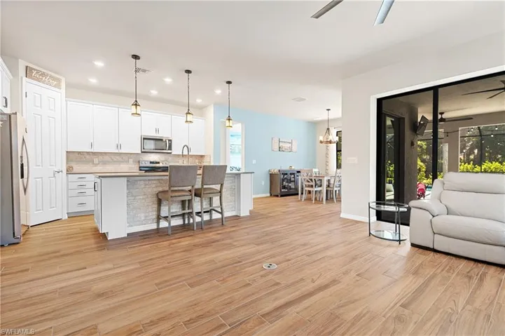 Kitchen with open floor plan, white cabinetry, ceiling fan, an island with sink, and appliances with stainless steel finishes