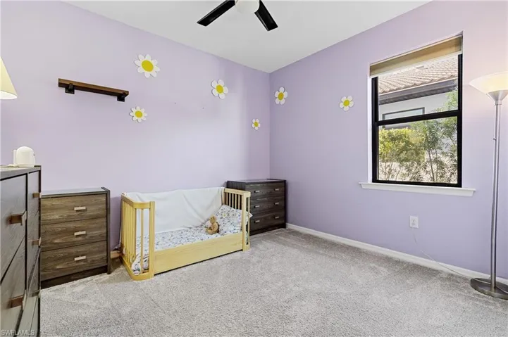 Unfurnished bedroom featuring light carpet, a nursery area, and ceiling fan