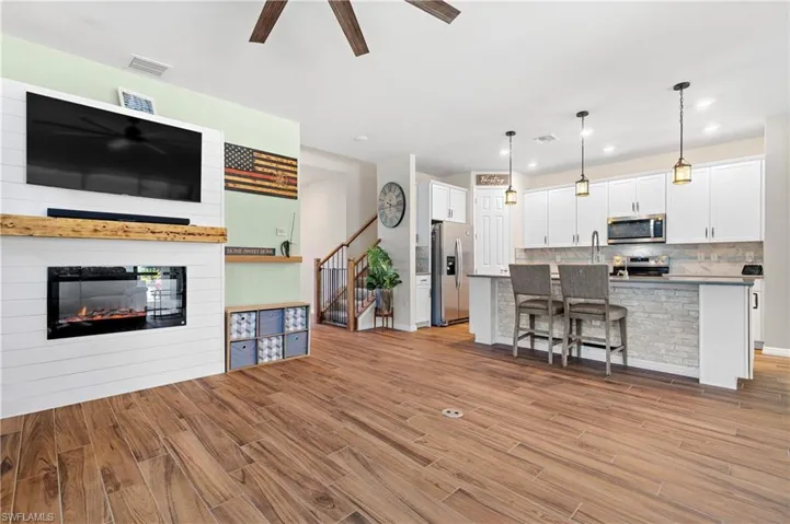 Living area with a ceiling fan, a glass covered fireplace, light wood-style flooring, and recessed lighting