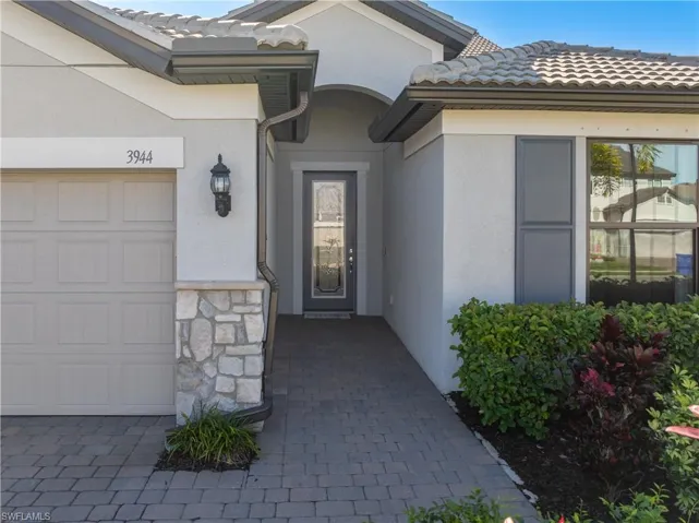 Entrance to property with a tile roof, stucco siding, stone siding, and a garage