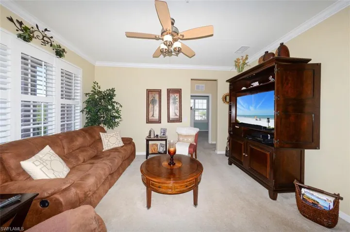 Spacious Great Room features 9'4" ceilings, Crown Molding, Plantation shutters, French door to Lanai and open to the Breakfast bar and Kitchen. Shows hallway leading to 2 guest bedrooms and a full bath.