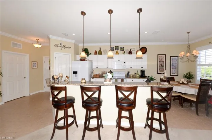 Open Kitchen shows tiled entry foyer to the left and features a Breakfast bar, pantry, 9'4" ceilings, Crown molding, recessed and pendant lighting, White cabinetry, beautiful Granite Countertops, Plantation shutters and Dining area to right.