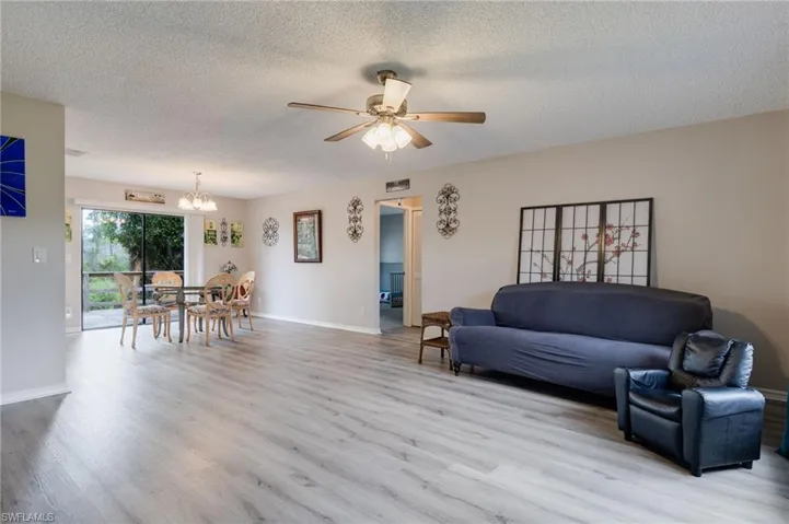 Living area with a textured ceiling, light wood-style floors, a chandelier, and ceiling fan