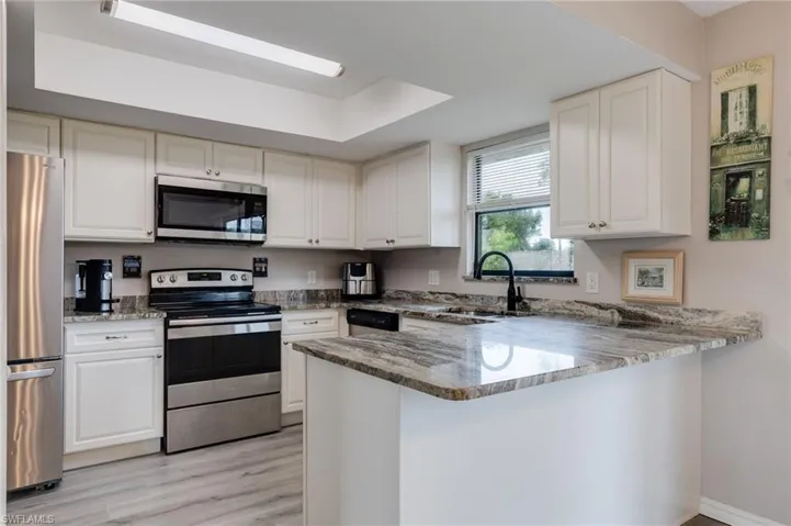 Kitchen with stainless steel appliances, a peninsula, light stone countertops, light wood-style floors, and white cabinets