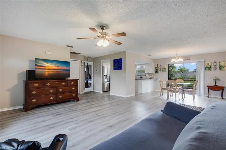 Living room with light wood finished floors, a textured ceiling, a chandelier, and ceiling fan