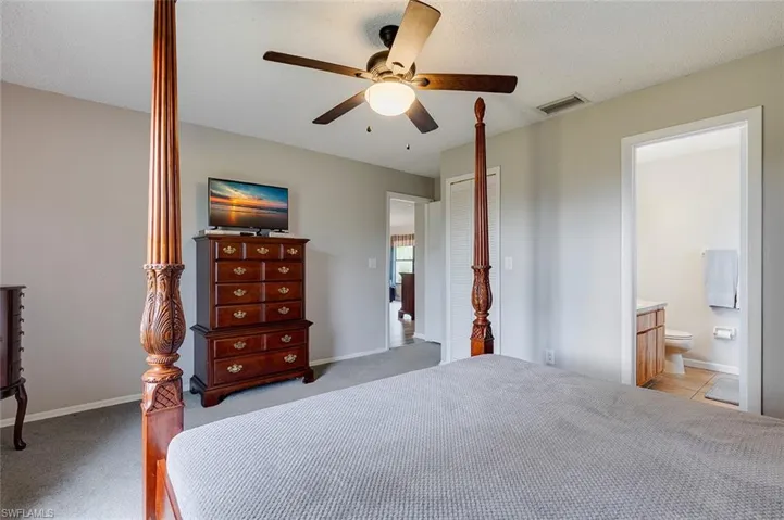 Bedroom with carpet, a textured ceiling, ceiling fan, and ensuite bath