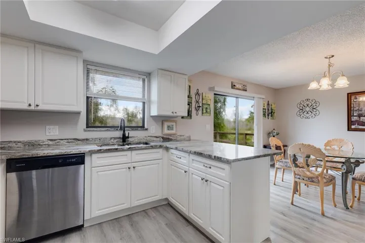 Kitchen with stainless steel dishwasher, a peninsula, white cabinets, light wood finished floors, and a chandelier