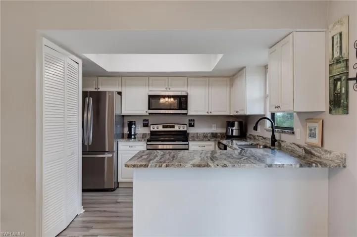 Kitchen featuring appliances with stainless steel finishes, light stone countertops, white cabinets, light wood-style flooring, and a peninsula