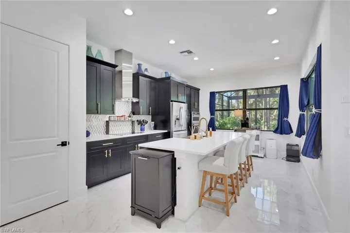 Kitchen with tasteful backsplash, light marble finish floors, dark cabinets, a breakfast bar, and recessed lighting