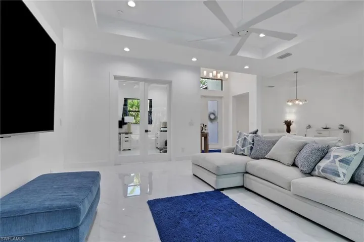 Living room with a raised ceiling, a chandelier, recessed lighting, marble tiled flooring, and french doors
