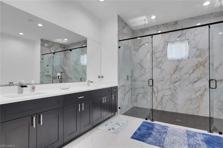 Bathroom with double vanity, light marble finish flooring, recessed lighting, and a marble finish shower