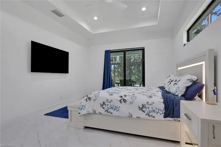 Bedroom with marble look tile flooring, a raised ceiling, recessed lighting, a ceiling fan, and access to outside
