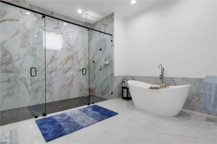 Full bathroom featuring tile walls, marble tiled floors, a wainscoted wall, a freestanding tub, and a marble finish shower