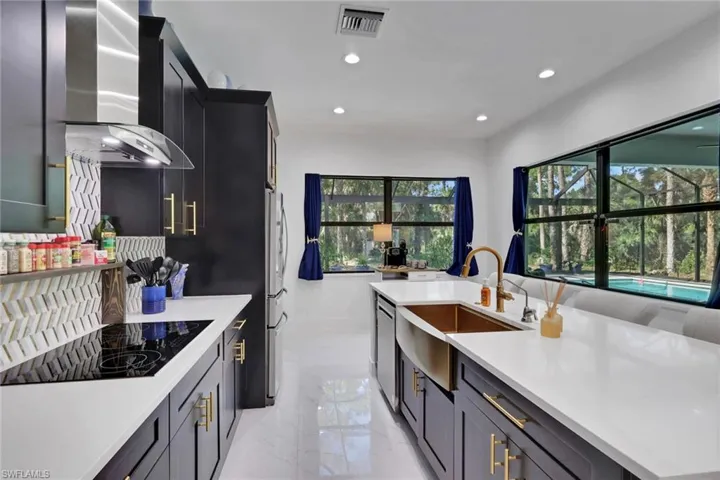 Kitchen with recessed lighting, wall chimney exhaust hood, black electric cooktop, light stone counters, and an island with sink