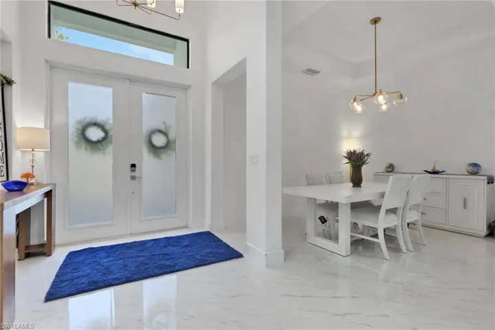Foyer with a chandelier, light marble finish flooring, french doors, and a towering ceiling