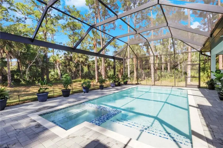 View of pool featuring glass enclosure, a pool with connected hot tub, a sunroom, and a patio