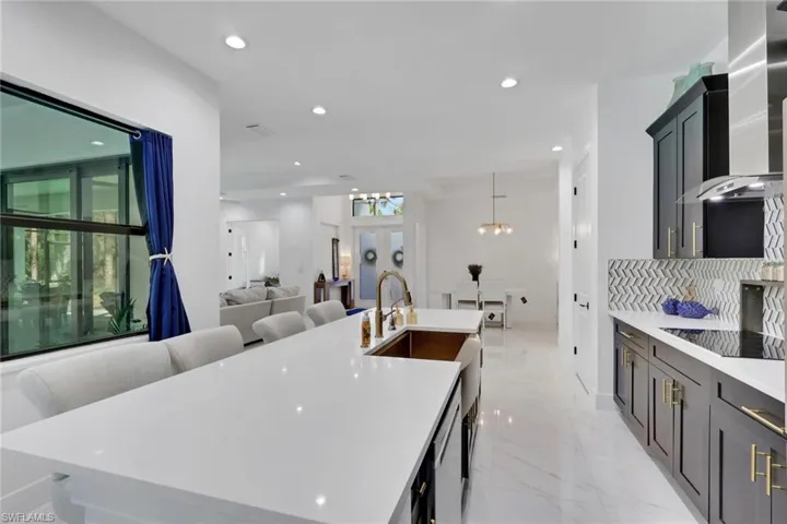 Kitchen with recessed lighting, open floor plan, wall chimney range hood, light stone counters, and an island with sink