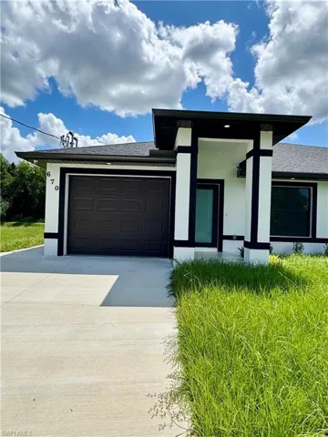 View of front facade featuring stucco siding, driveway, roof with shingles, and an attached garage