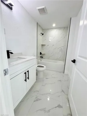 Bathroom with tub / shower combination, vanity, a textured ceiling, and light marble finish floors