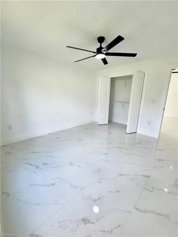 Unfurnished bedroom featuring light marble finish flooring, a ceiling fan, and a closet