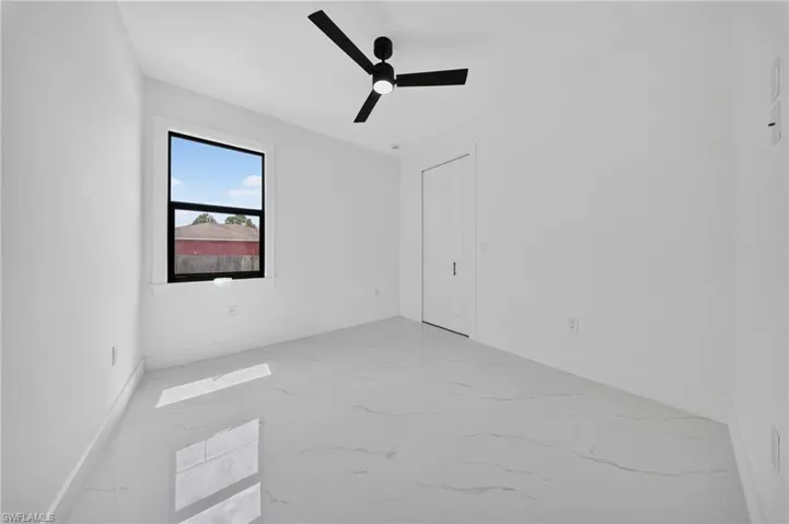 Bright interior space featuring large format tile flooring, a contemporary black ceiling fan, and a single window with black trim