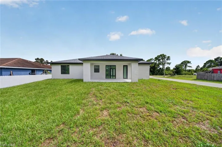 Rear exterior featuring a white stucco finish, dark-framed windows, and a covered patio area