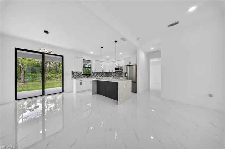Open-concept interior featuring large format marble-look tile flooring, white shaker cabinetry, an island with a waterfall-edge countertop, stainless steel appliances, and sliding glass doors to the exterior
