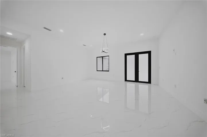Spacious room featuring large format marble-look tile flooring, white walls, recessed lighting, and a contemporary chandelier