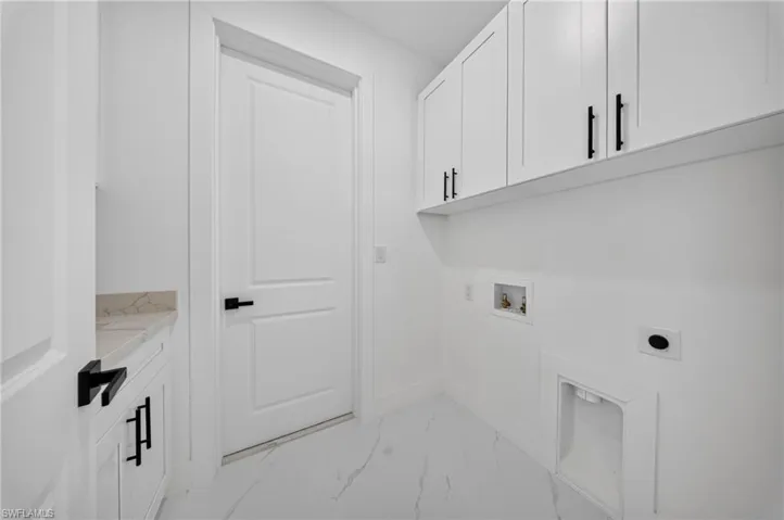 White laundry room featuring upper cabinetry with matte black hardware, a light-toned countertop, and white tile flooring