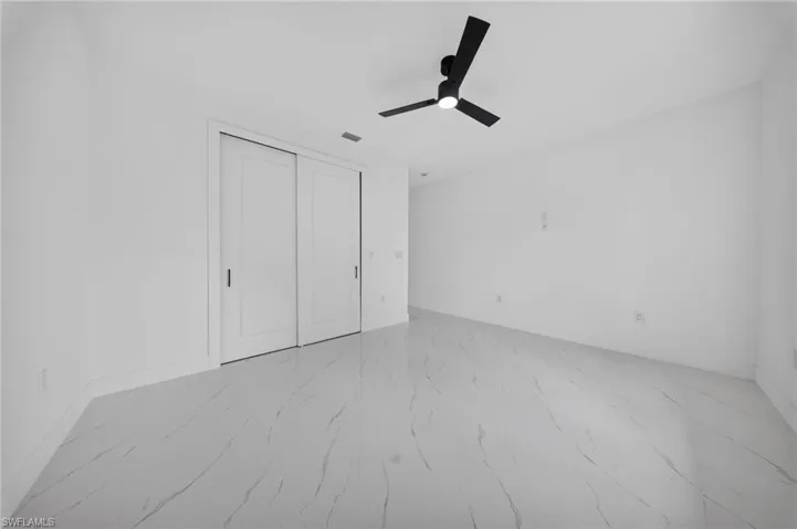 Spacious interior room featuring white walls, large format tile flooring, and a contemporary black ceiling fan