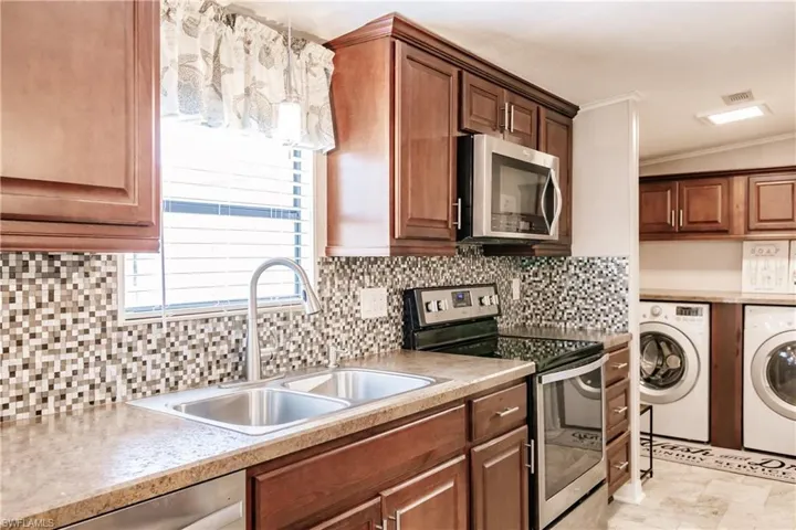 Kitchen with light tile patterned floors, stainless steel appliances, washing machine and clothes dryer, pendant lighting, and sink