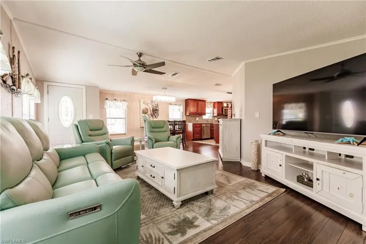 Living room with dark wood-type flooring, ornamental molding, and ceiling fan