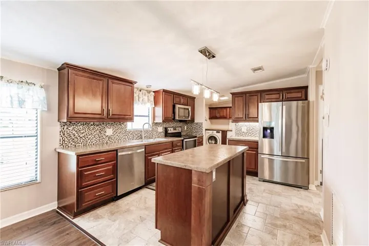Kitchen featuring appliances with stainless steel finishes, light tile patterned flooring, a center island, and decorative backsplash