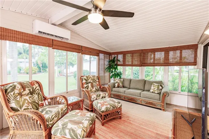Sunroom with lofted ceiling with beams, a wall mounted AC, and ceiling fan